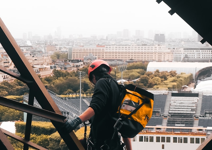 Ouvrier casqué travaillant sur la structure métallique de la tour Eiffel, avec Paris en arrière-plan
