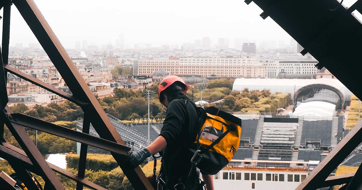 Ouvrier casqué travaillant sur la structure métallique de la tour Eiffel, avec Paris en arrière-plan
